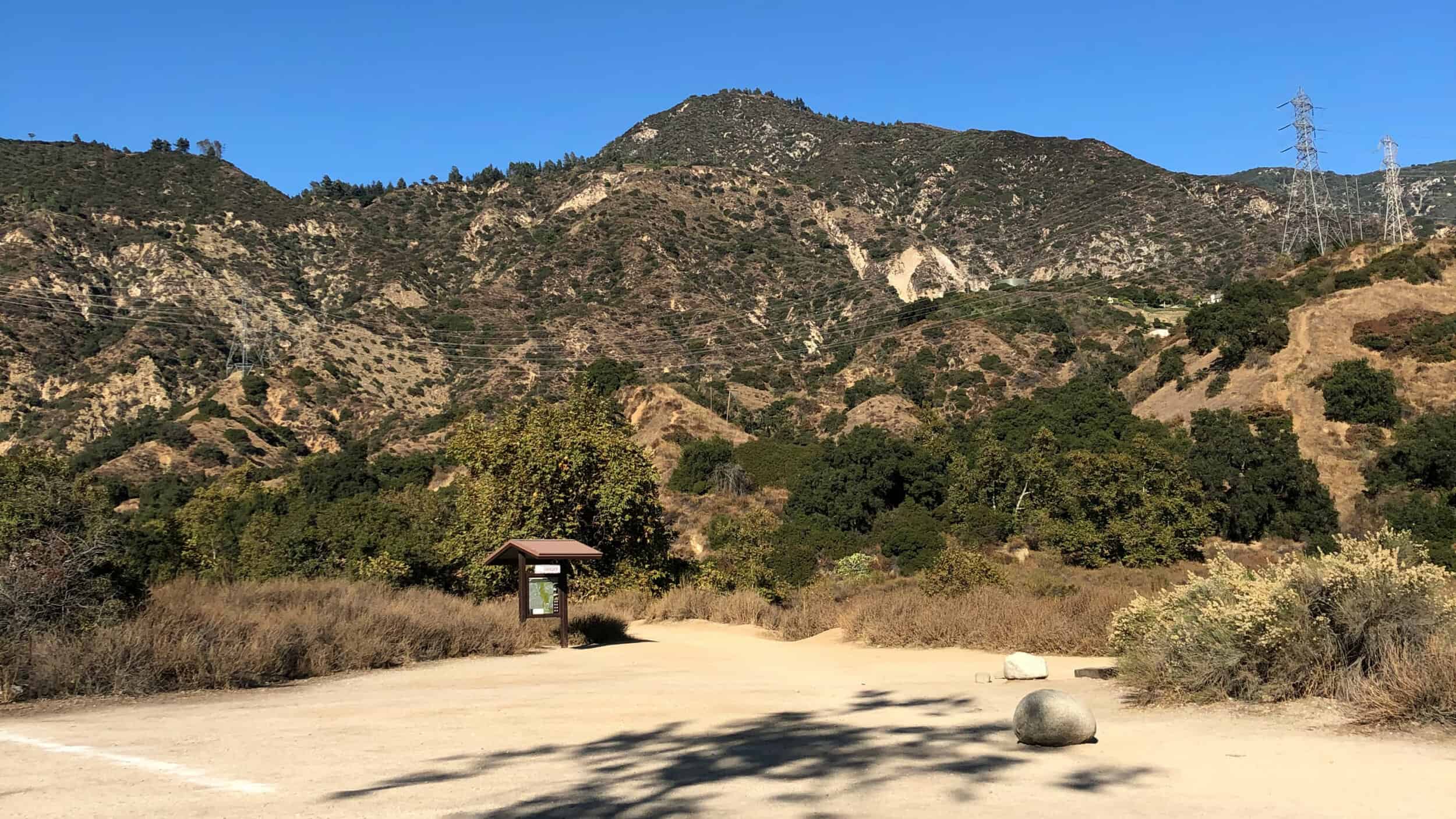 trail kiosk in front of dusty trail and desert mountain