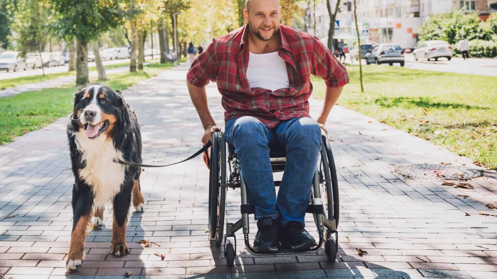 Happy young man with a physical disability who uses wheelchair with his dog.